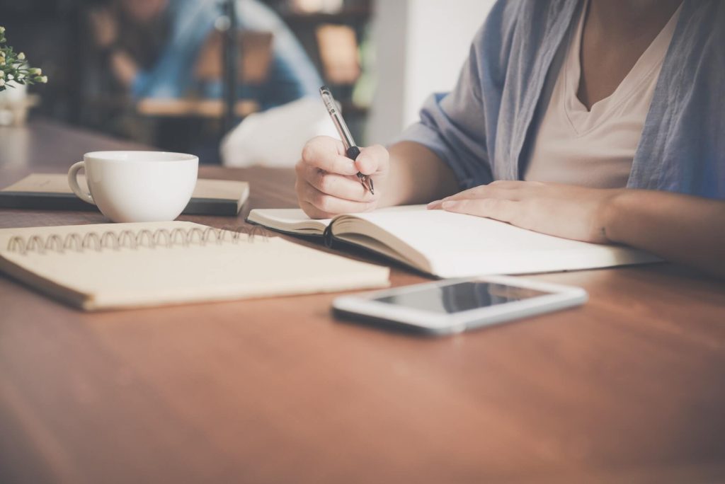 lady writing on her book at a coffee shop without revealing her face