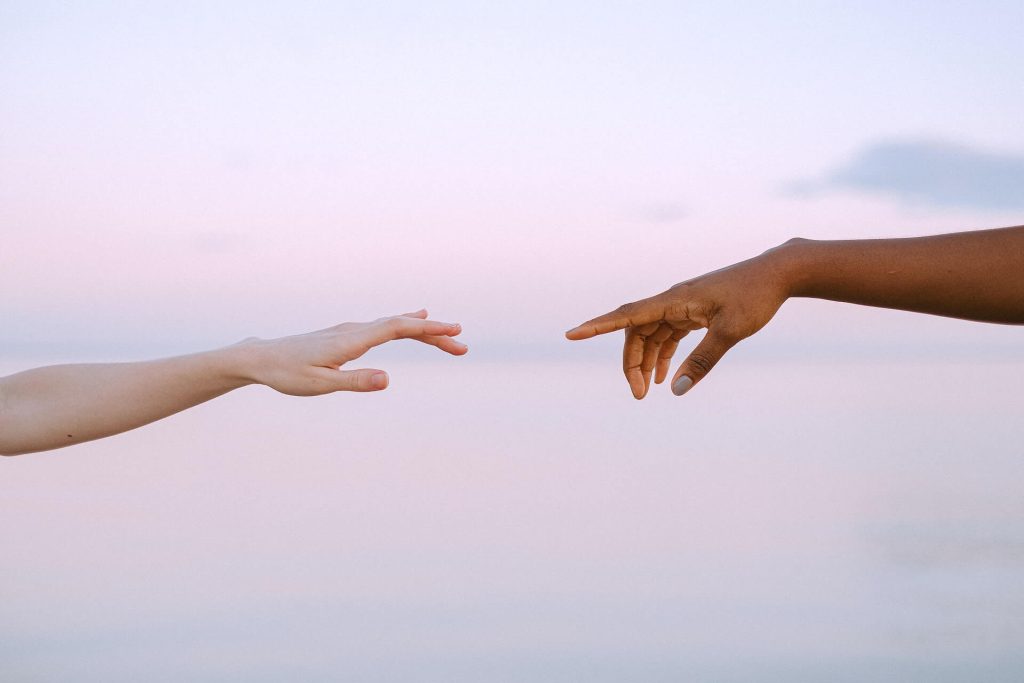 Two hands reaching out to each another to show trust and integrity by the sunset with a sea background